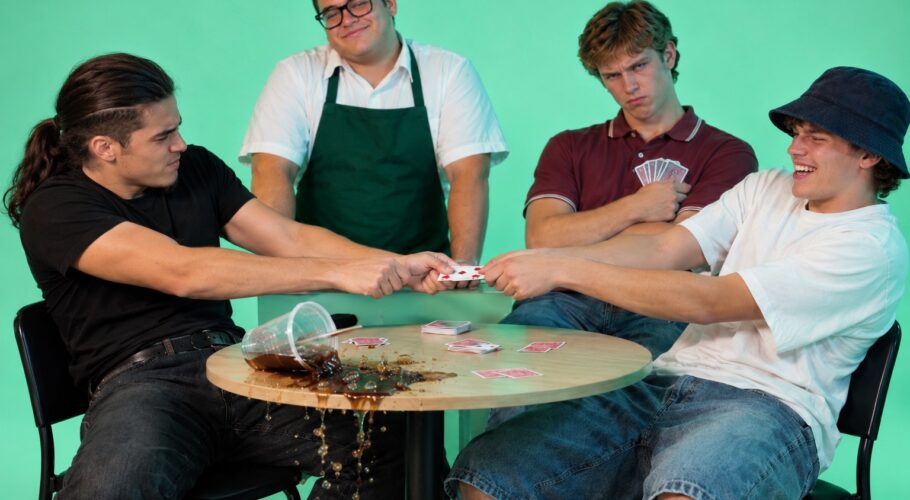 Tony in a black tee and a friend tugging a playing card over a spilled drink while a waiter watches, April 1999