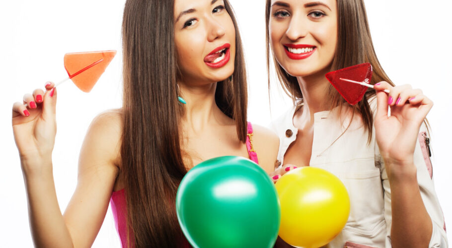 two happy girls smiling holding colored balloons and candy