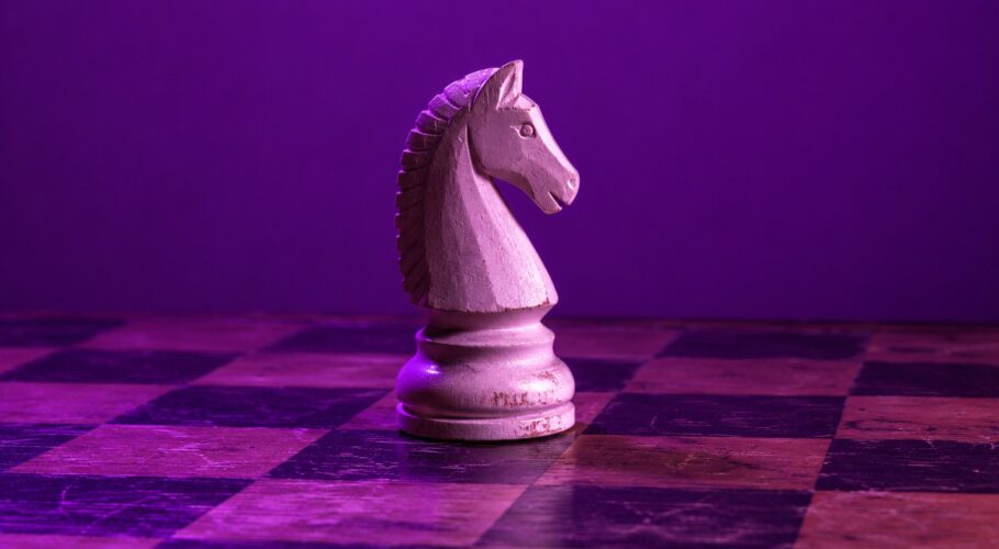 A white wooden chess knight on a chess board under purple light