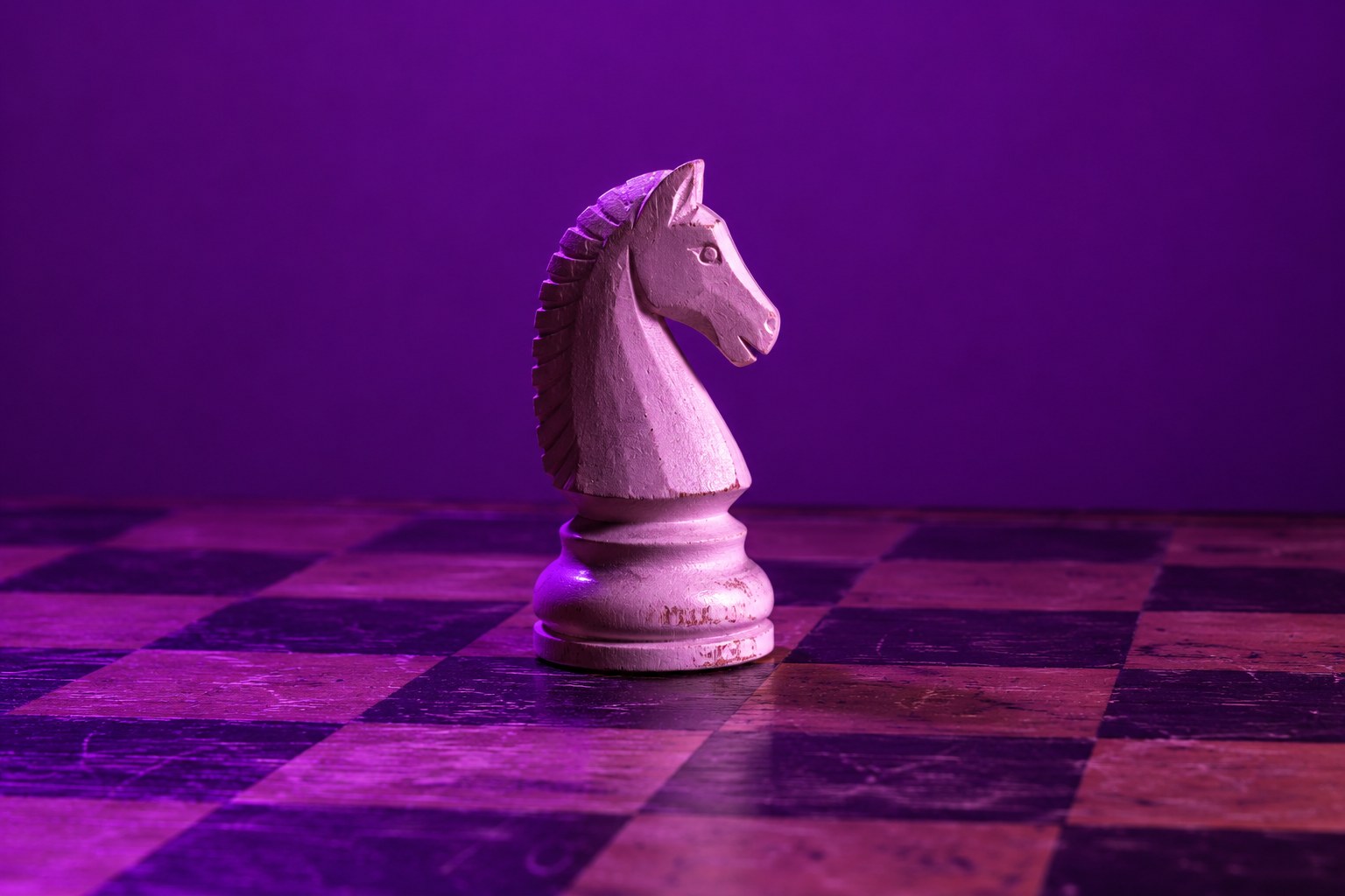 A white wooden chess knight on a chess board under purple light