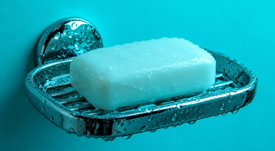 a white bar of soap on a wet chrome soap dish photographed in a studio
