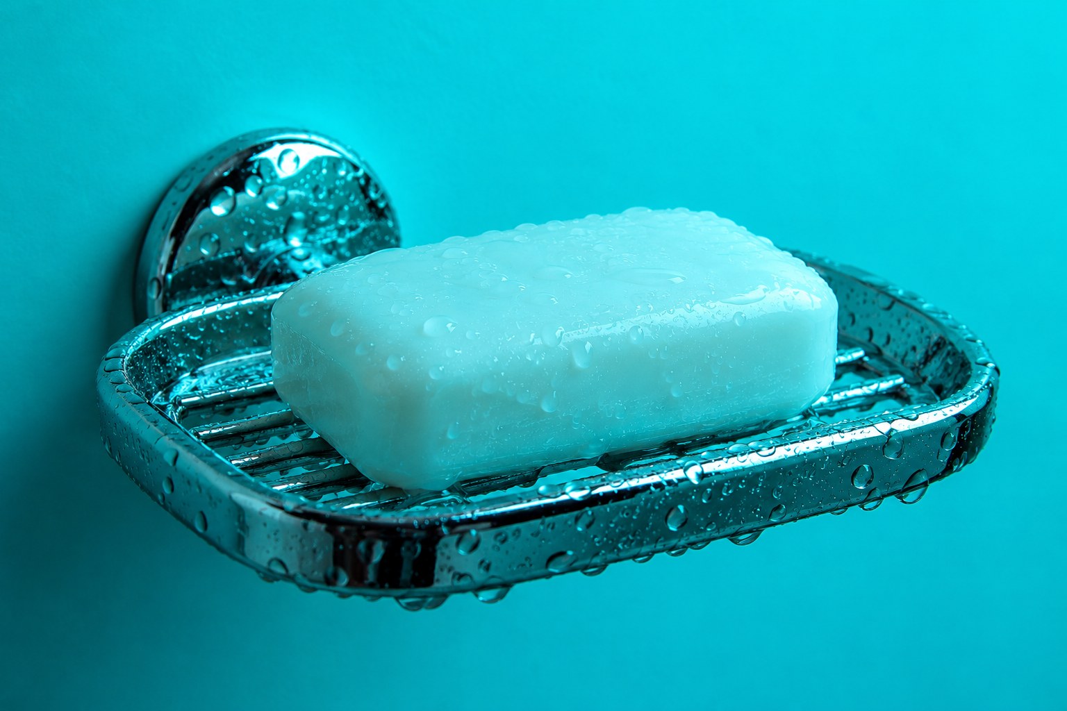 a white bar of soap on a wet chrome soap dish photographed in a studio