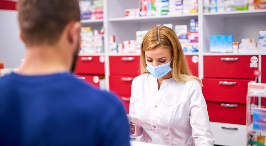 young female chemist cashier with protective medical face mask and young caucasian male customer buying drugs