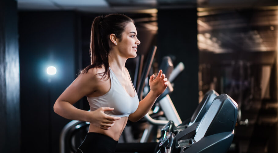 young sports woman with ponytail working out gym running treadmill side view