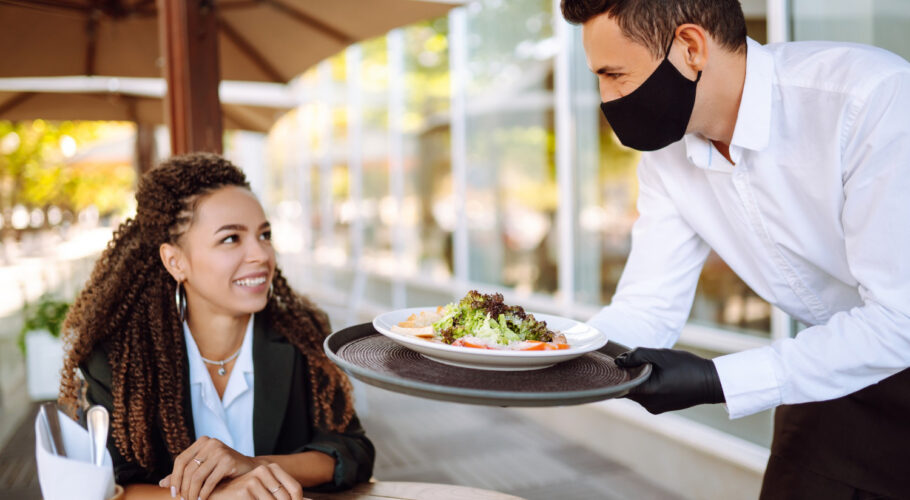 young waiter in a protective face mask wearing gloves with ordered meals ready to serve