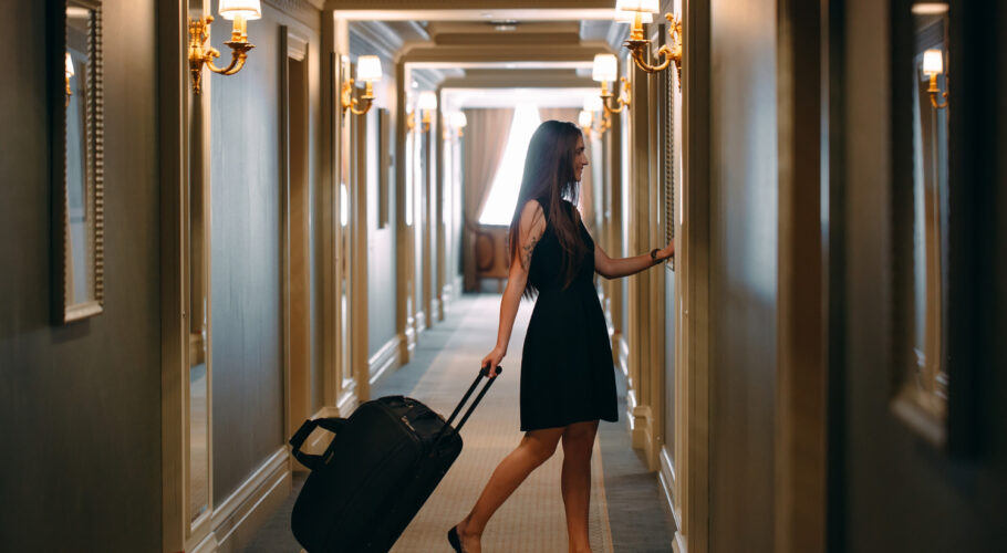 young elegant woman with handbag and suitcase walks down hotel corridor to her room